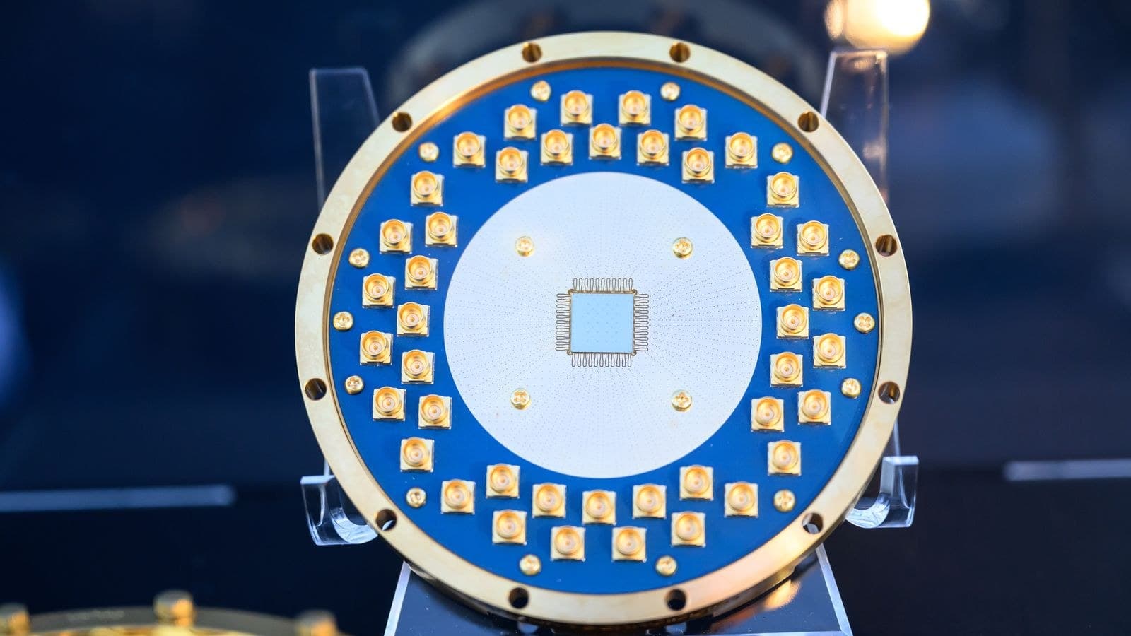An Anyon Computing superconducting quantum processor chip at the center of a blue circuit board ringed with gold-plated connectors
